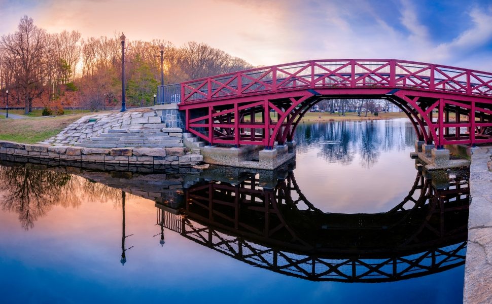 Arching Pink Wooden Bridge and Reflections over the pond at Elm Park in Worcester, Massachusetts. Tranquil Sunset Landscape over the Mirror Like Lake